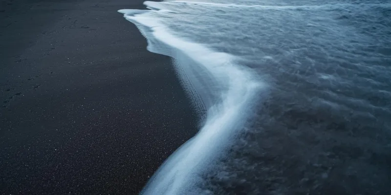 Dark sand beach with wave edge — the retention boundary where churn erodes growth